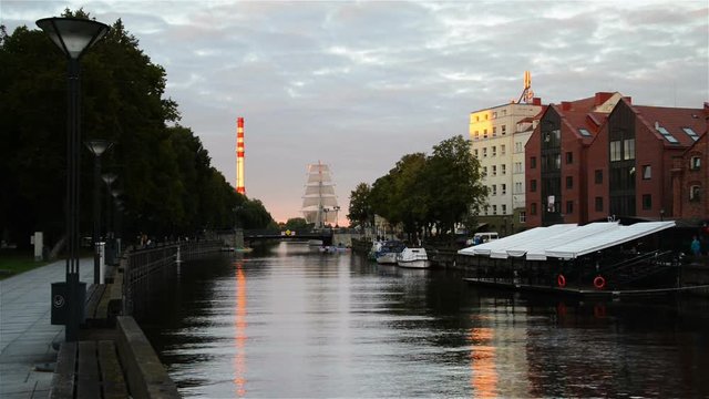 View of the Dane river quay in the evening in Klaipeda, Lithuania. Sunset sky with various cafes and restaurants. Embankment area and ship at the background