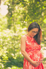 Young pregnant woman in the park at summer day