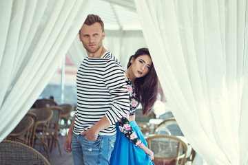 Beautiful young fashion stylish couple walking on the street near the white cafe together in summer...