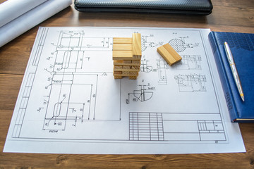 The man (businessman, architect) draws a plan, graph, design on large sheet of paper at office desk and builds model house from wooden blocks 