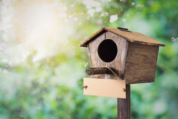 old wooden birdhouse and hanging blank signboard with blurred sunrise behind the bush