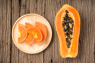 top view of ripe papaya pieces in wood dish and the half fruit on old wood