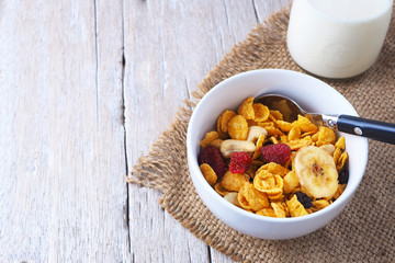Close up of a healthy bowl of corn flakes breakfast cereal topped with dried fruits and nuts on a wooden table.