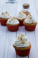 Cupcakes with mascarpone cream and gold decoration on a white wooden table.