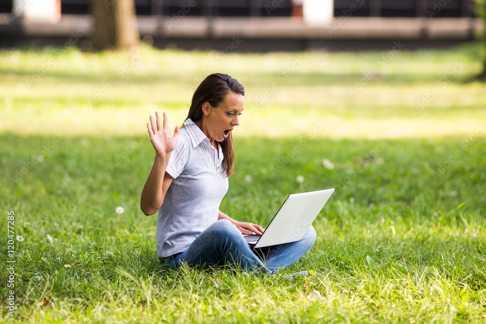 Wall mural businesswoman sitting at the park and looking at her laptop in panic.