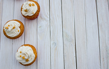 Cupcakes with mascarpone cream and gold decoration on a white wooden table.