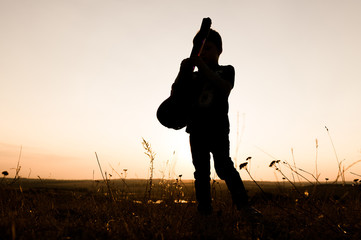 silhouette of boy with guitar at sunset 