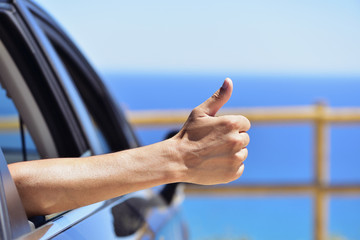 man giving a thumbs up sign in a car near the ocean