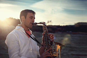elegant man play the saxophone on beach in warm  day