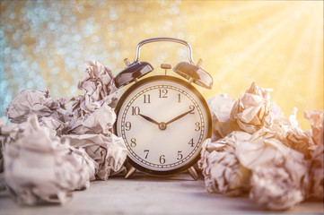 Alarm clock in a wastepaper concept for a time waste of time with golden bokeh blur texture background
