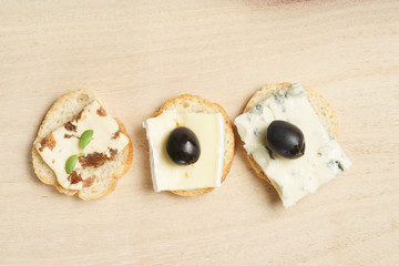 Various types of cheese with rusks and olives on wood background