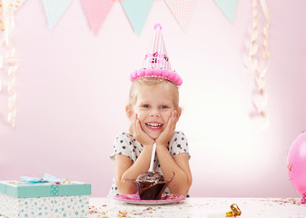 Joyful little girl having birthday party at home. Cute kid with gift box and cupcake in the room. - 120481429
