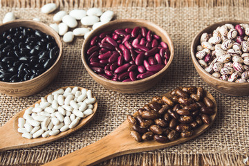 Beautiful multi-colored beans in bowls and wooden spoons on a background of burlap