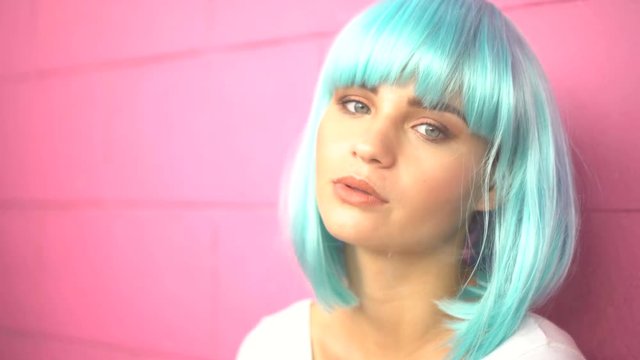 4k video of sexy young girl in modern futuristic style with blue wig smoking e-cigarette and puffing out cloud of smoke over pink wall background