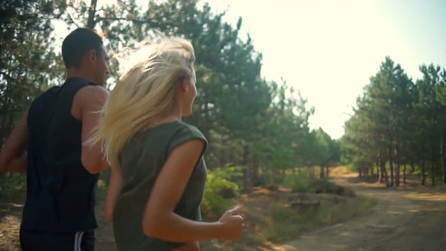 Young sportive couple jogging along path in forest Slow motion Back view