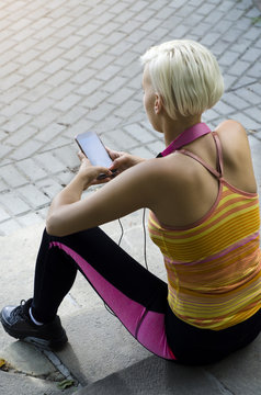 Young Athletic Woman Sitting On Stairs Looking At Smart Phone, Back View