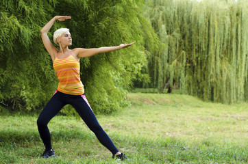 Young, fit, beautiful woman doing Tai Chi pose in park outdoors
