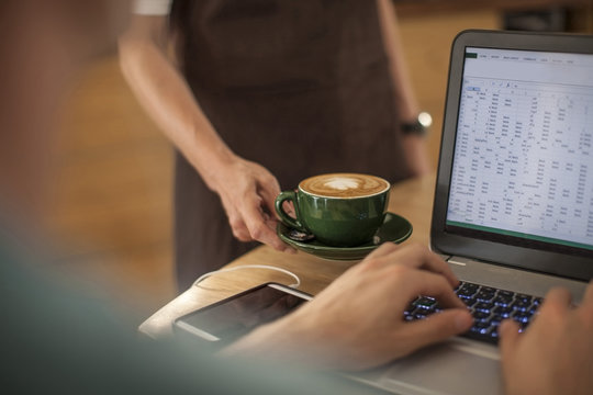 Waitress serving coffee to man in a cafe working on laptop