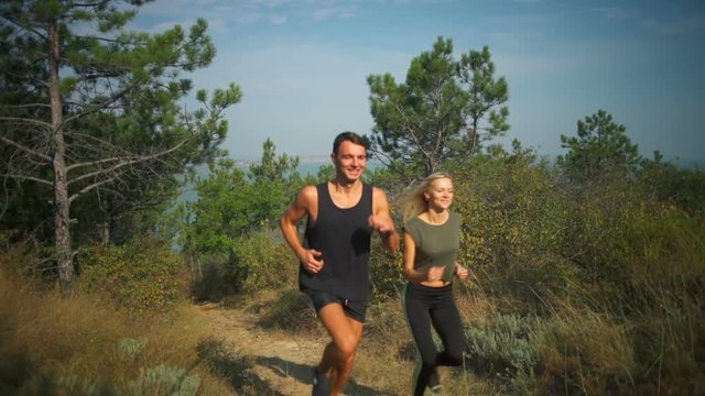 Sportive couple smiling jogging up on hill firth background Slow motion
