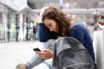 Serious young woman sitting and using mobile phone