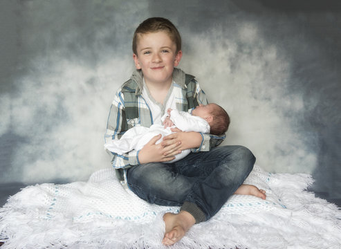 Family portrait image of a young boy holding a newborn baby. 