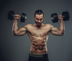 Fototapeta na wymiar A man holds dumbbells with arms up on grey background.