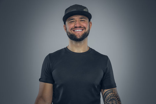 Bearded male in a baseball cap on grey background.