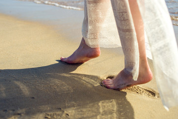 girl walks barefoot on the sand in a white dress
