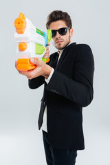 Fototapeta premium Focused businessman in sunglasses and suit shooting with water gun