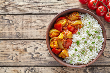 Chicken jalfrezi traditional Indian spicy curry chilli meat with basmati rice and vegetables healthy dietetic asian food in clay dish on vintage table background.