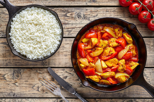 Chicken jalfrezi dietetic traditional Indian curry spicy fried meat with vegetables and basmati rice asian food in cast iron pan on vintage table background