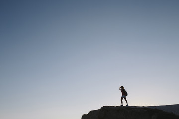 silhouette young woman tourist with backpack standing on cliff