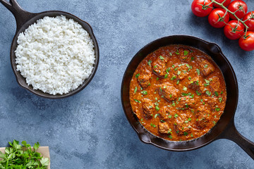 Madras butter Beef spicy slow cook lamb food with rice and tomatoes in cast iron pan on blue table...