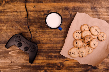 Gamepad and homemade chocolate chip cookies on rustic wooden tab
