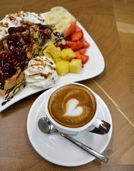 Cup of foamy cappuccino and waffles with fruit and whipped cream