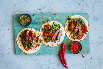 Healthy lunch snack. Mexican tortilla wraps with grilled beef steak, salsa verde and vegetables.