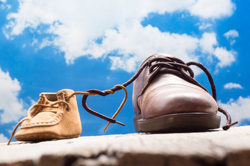 father and child shoes on wood with clouds and sky background tie the shoestring together in heart shape, love and bound concept