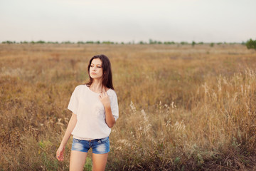 Fototapeta na wymiar Young girl with long brown hair standing at the autumn meadow