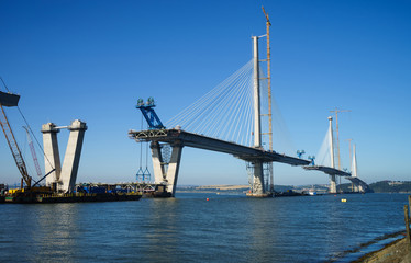 The new Queensferry Crossing Bridge under construction, seen from Port Edgar (Edinburgh, Scotland).  Showing a mobile crane used for lifting new sections of the deck from barges, and bridge piers.