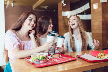 Three cheerful young girls eating fast food in a restaurant