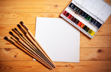 Watercolor paints, brushes for painting and paper sheet on  wooden  background