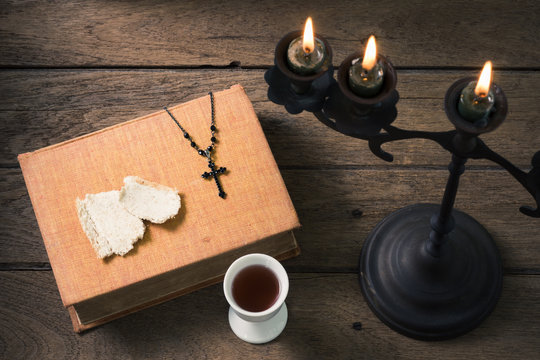 still life photography : bible, crucifix, bread and chalice of wine with candelabrum at foreground on old wood table
