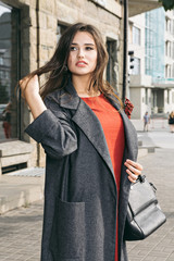 Fashion portrait of beautiful sexy woman Wearing a fashionable orange dress, grey coat. Posing on a city street