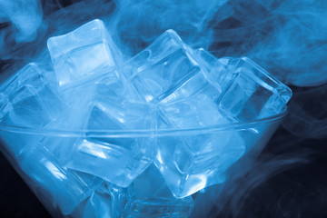 Cloud of smoke over martini glass with ice cubes on black backgr