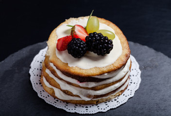 Biscuit homemade cake with cream and berries on black background