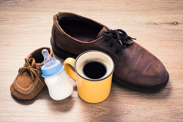 coffee cup in father shoes and milk bottle in child shoes, love and bound concept