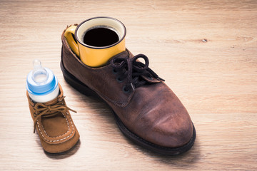 coffee cup in father shoes and milk bottle in child shoes, love and bound concept