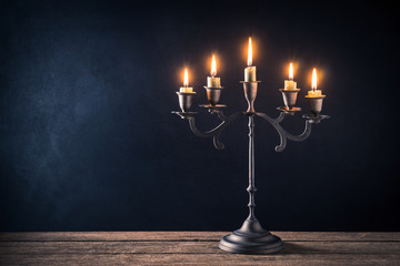 handicraft candelabrum with burning candles on old wooden table against art dark background - obrazy, fototapety, plakaty