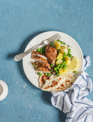 Lemon thyme baked chicken, potatoes and green peas on a white plate on a blue background. Delicious lunch