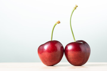 two of fresh red cherries on wooden table against bright background